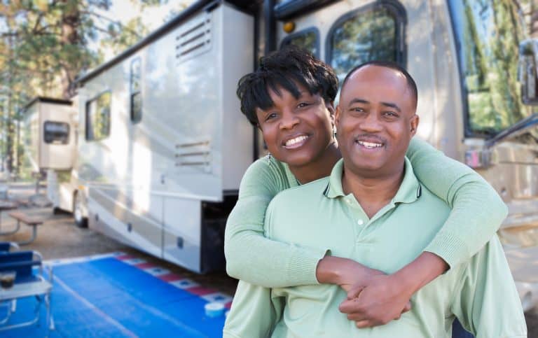 Couple stands outside their motorhome at camp site.
