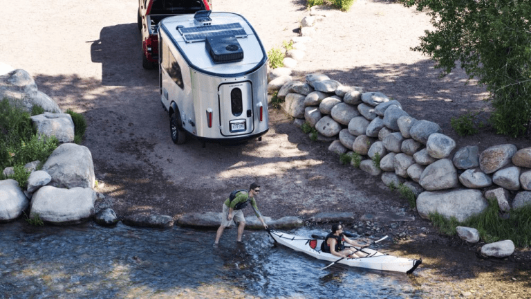 Small travel trailer on boat ramp with kayakers.