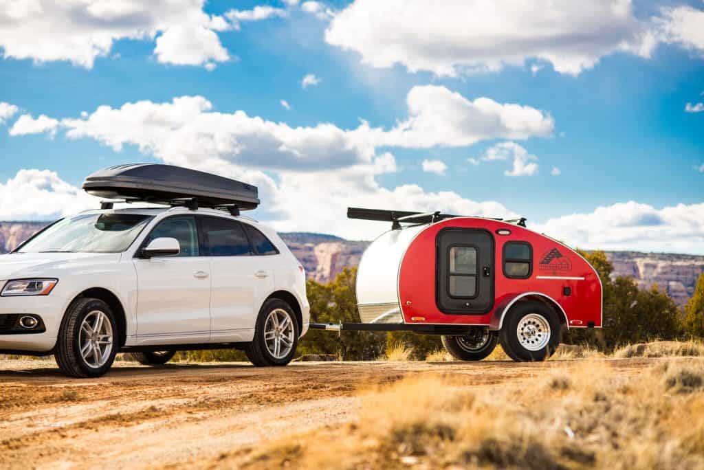 SUV pulls small teardrop travel trailer on dirt road.