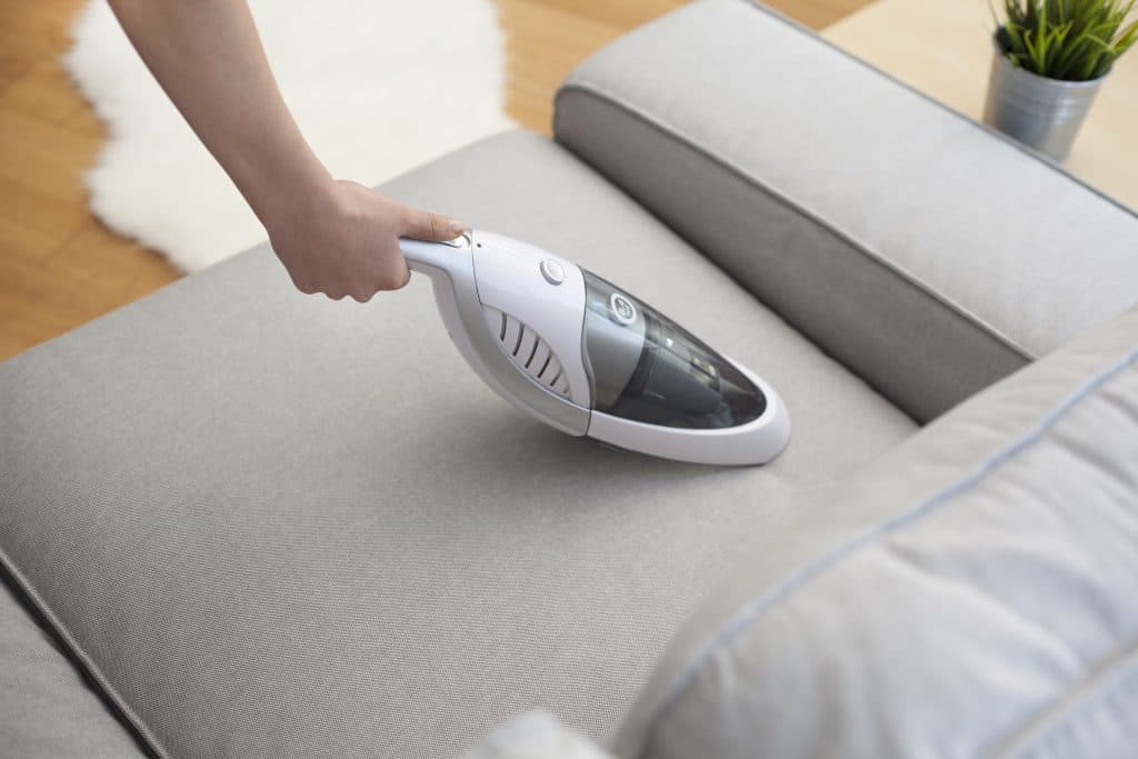 A hand holds a portable vacuum to clean furniture.