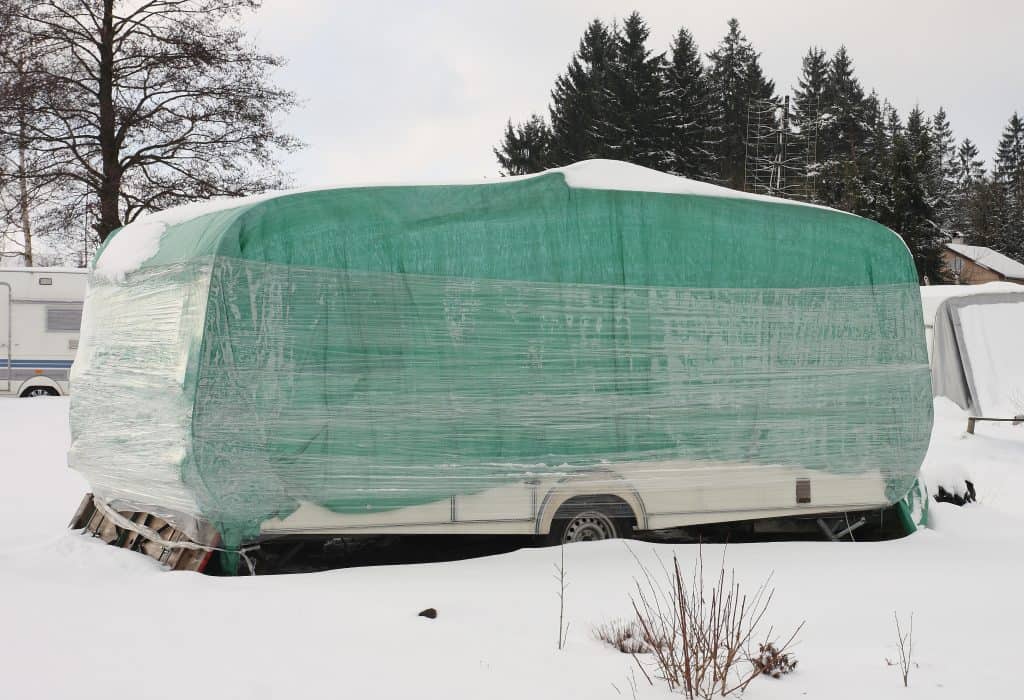 Travel trailer with makeshift cover in outdoor storage in winter.