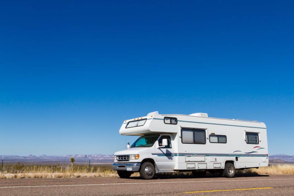 Class C motorhome pulled over on highway surrounded by flat landscape.