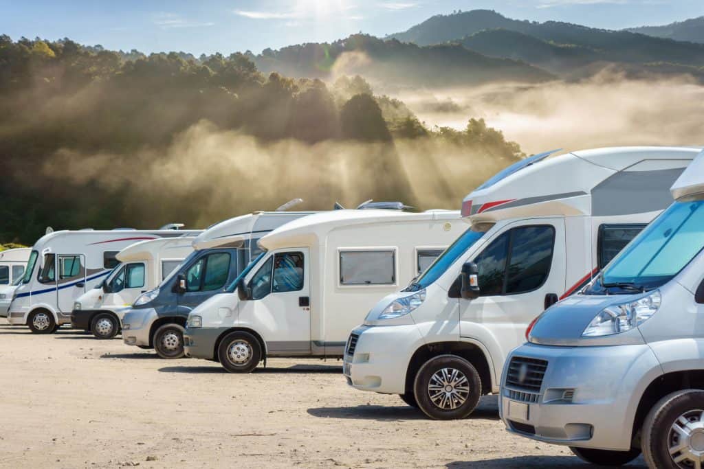 Small RVs parked in a row on a gravel lot.