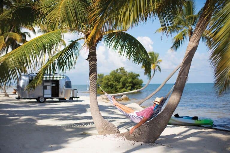 RVer swings from hammock between two palm trees on the beach.