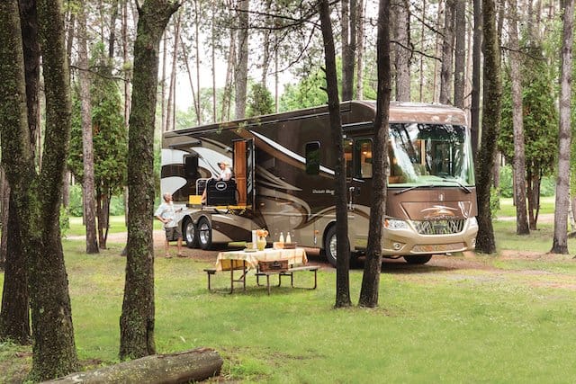 Handicap accessible motorhome at camp lowering wheelchair to ground.