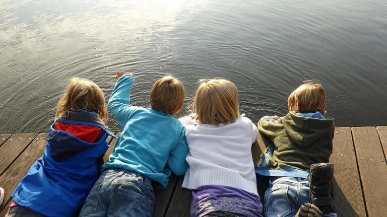 Kids lay on a dock and look into the lake.