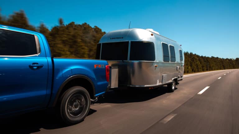 Blue pickup pulls airstream camper on highway.