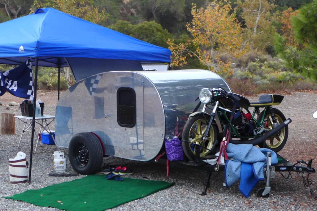 Campsite with very small teardrop camper and motorcycle.