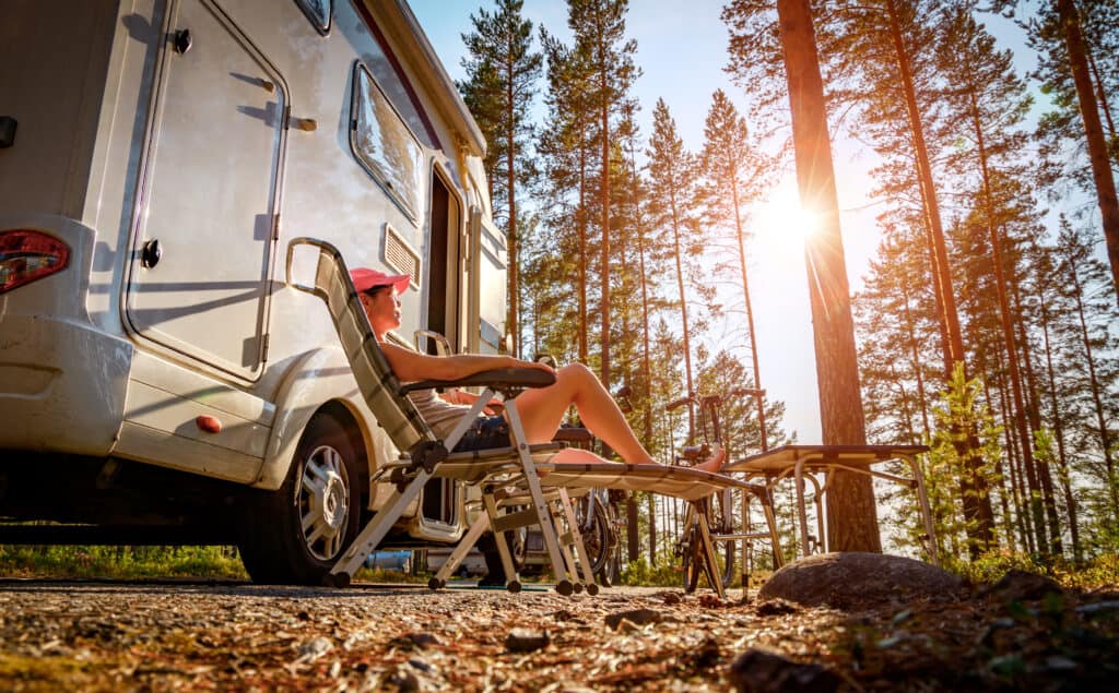 Woman relaxes in front of camper in secluded area.