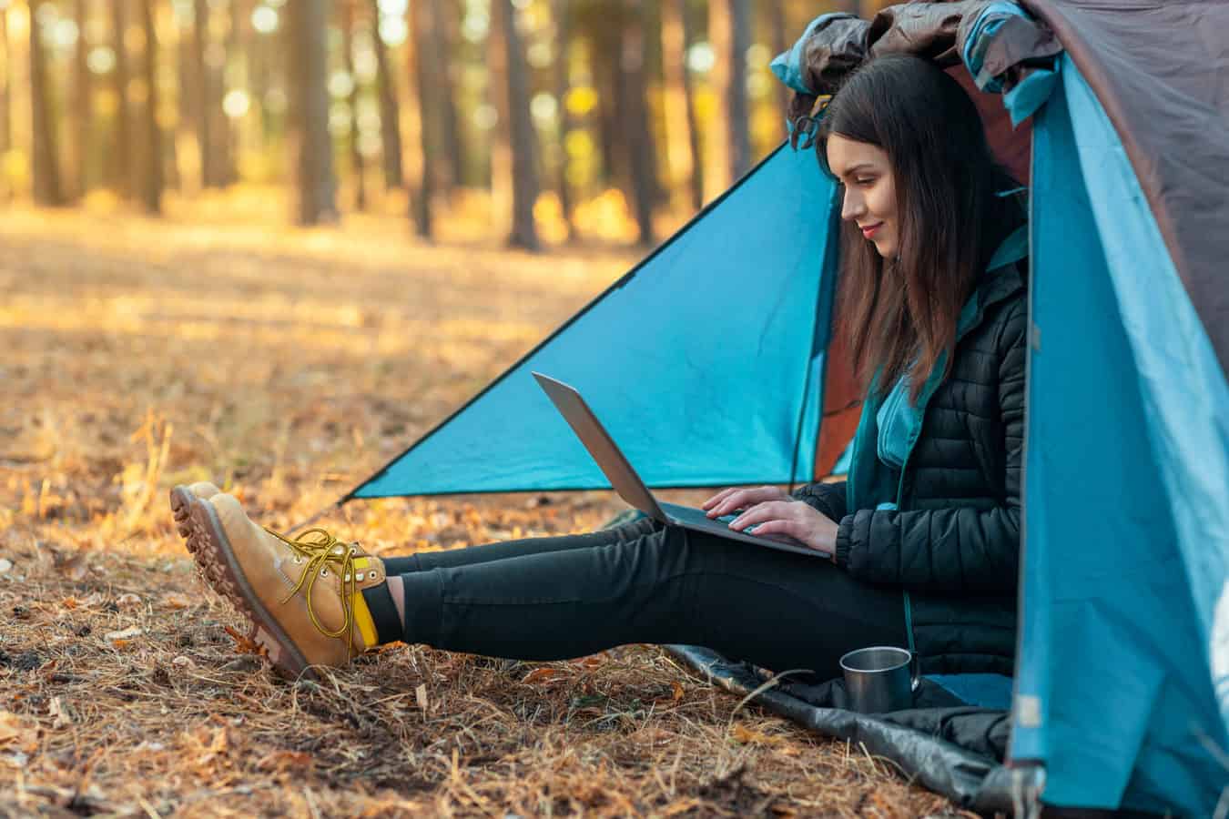 Women uses laptop outside while tent camping.