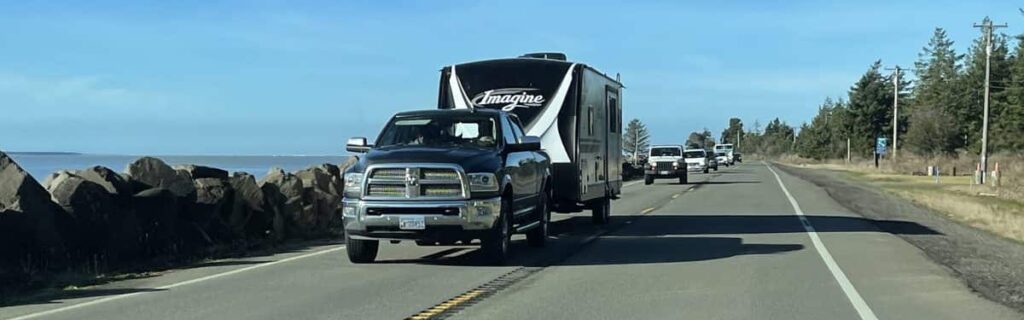A travel trailer being towed by a dark colored truck.