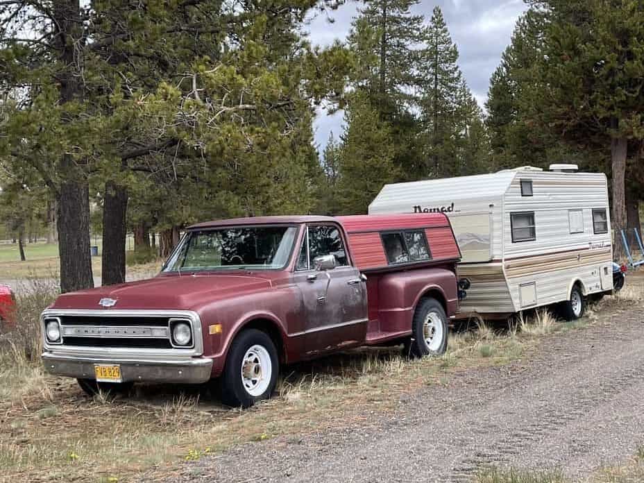 An old red truck and an older small travel trailer hooked together.