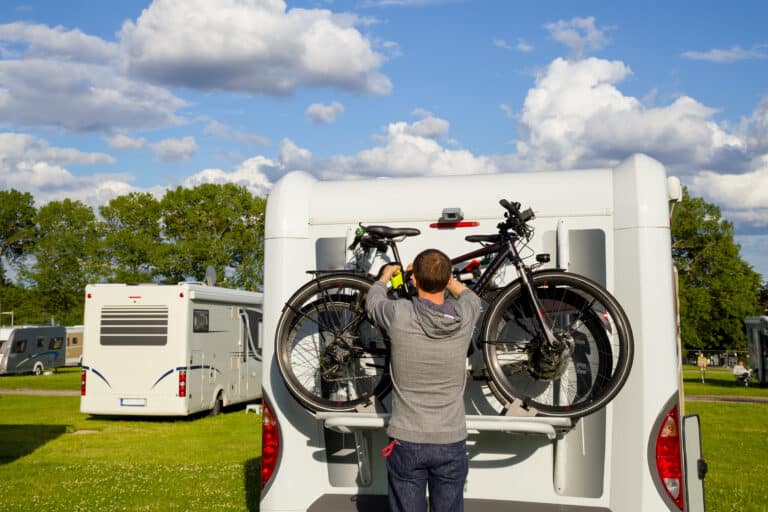 Man hangs bikes equipped with a GPS tracker on back end of an RV