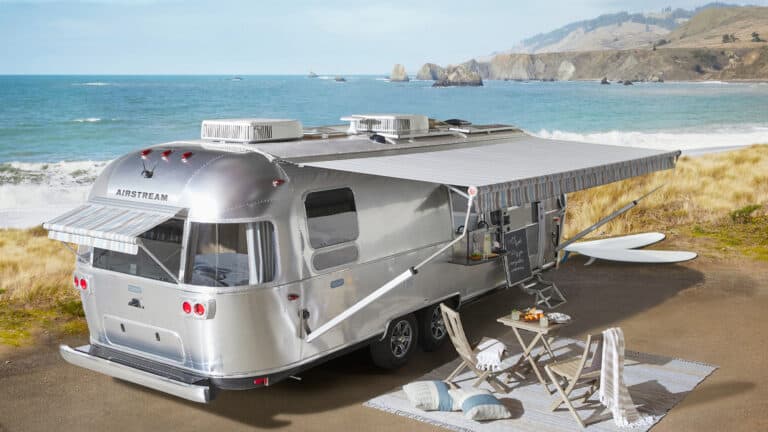 2022 Airstream Pottery Barn Special Edition travel trailer sitting infront of a beachfront with awning extended and featuring an outdoor seating arrangement-lounge chairs and table