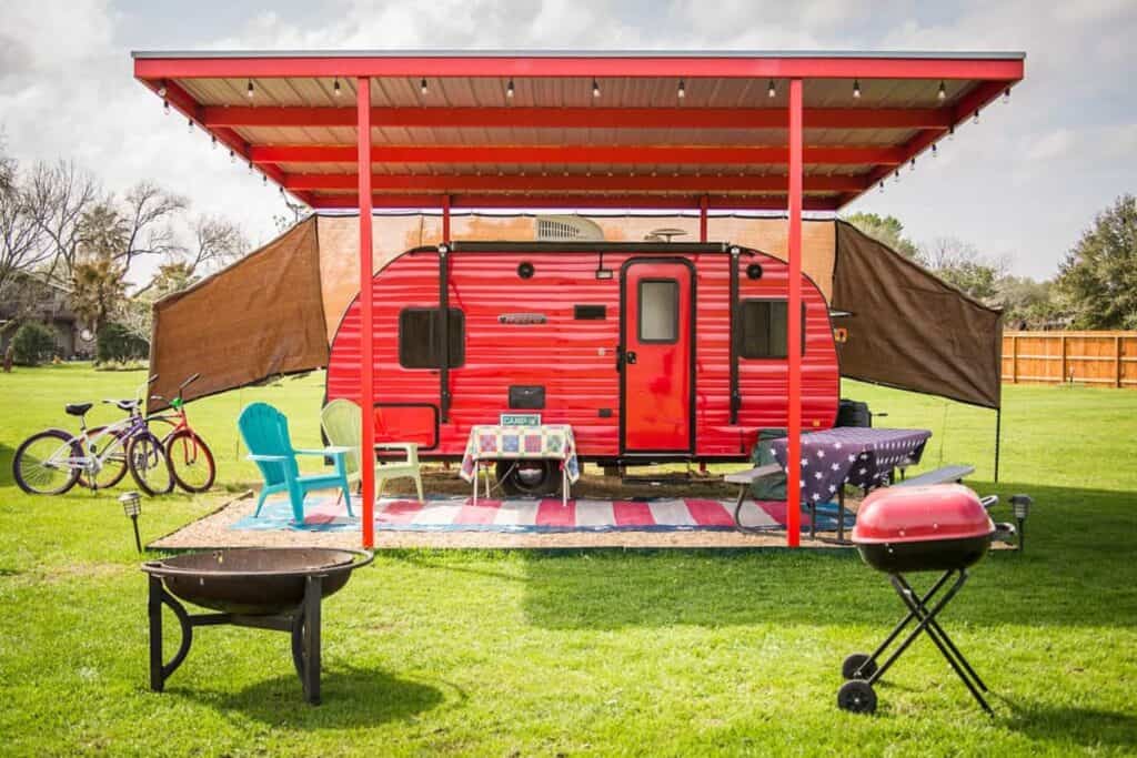 Bright red camper with a covered porch in a green field - RV Airbnb