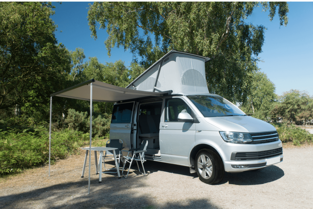 Camper van at a campsite with awning sset up over table and chairs - RV van rental