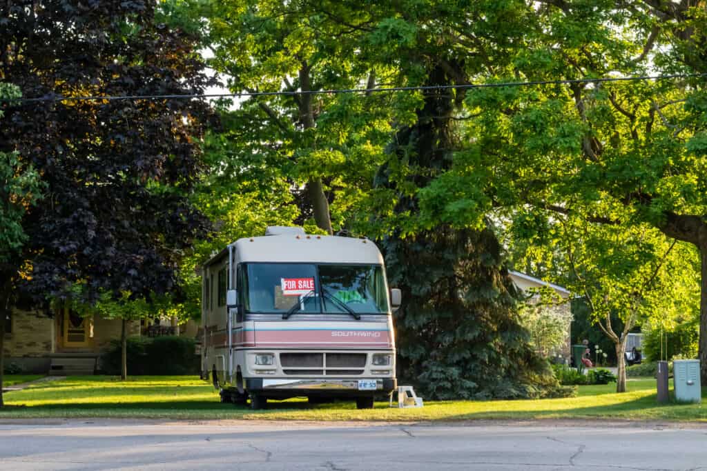 Older class A motorhome for sale on front lawn of treed property - RV consignment