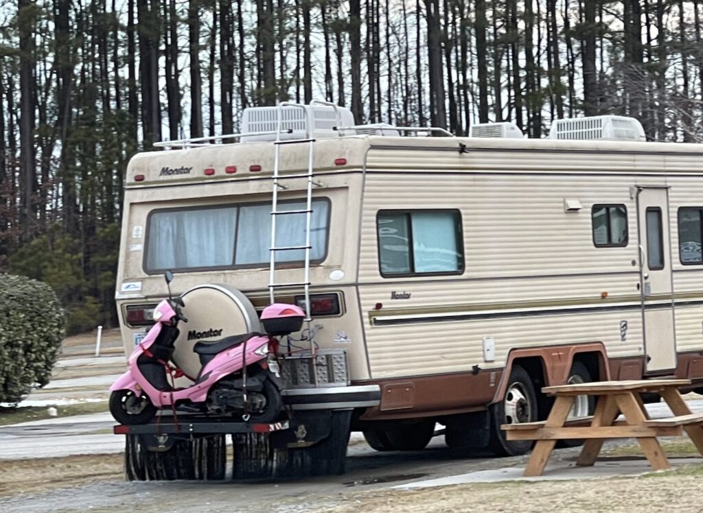 An older motorhome with a flip down storage rack carrying a pink moped