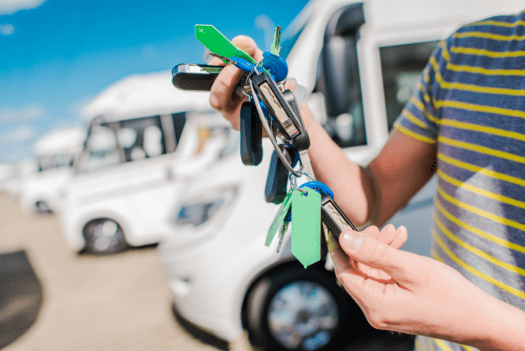 Someone holding a ring of RV keys at an RV dealership, with RVs in the background