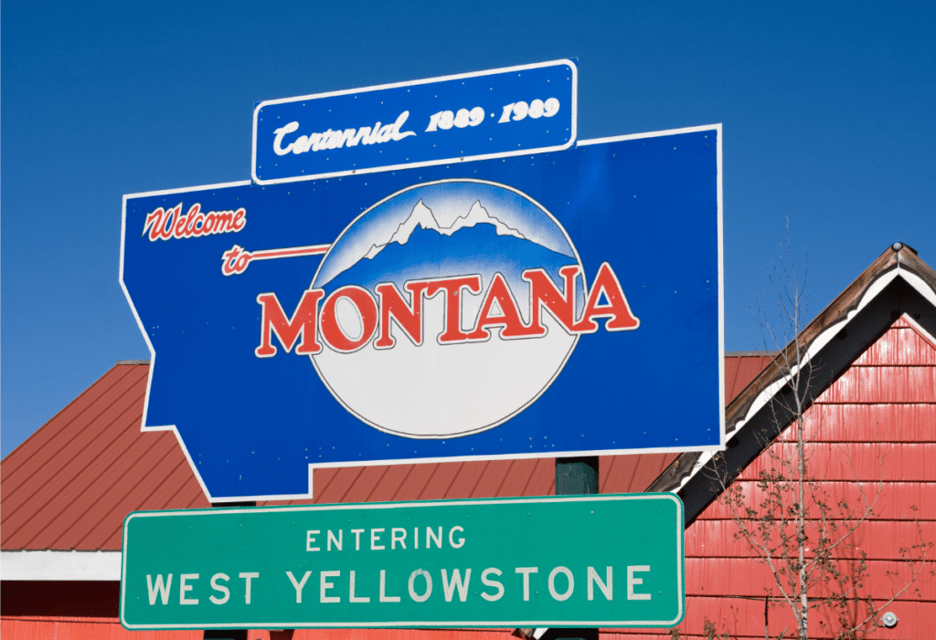 A blue road sign reading “Welcome to Montana,” with a green sign below it reading “Entering West Yellowstone”
