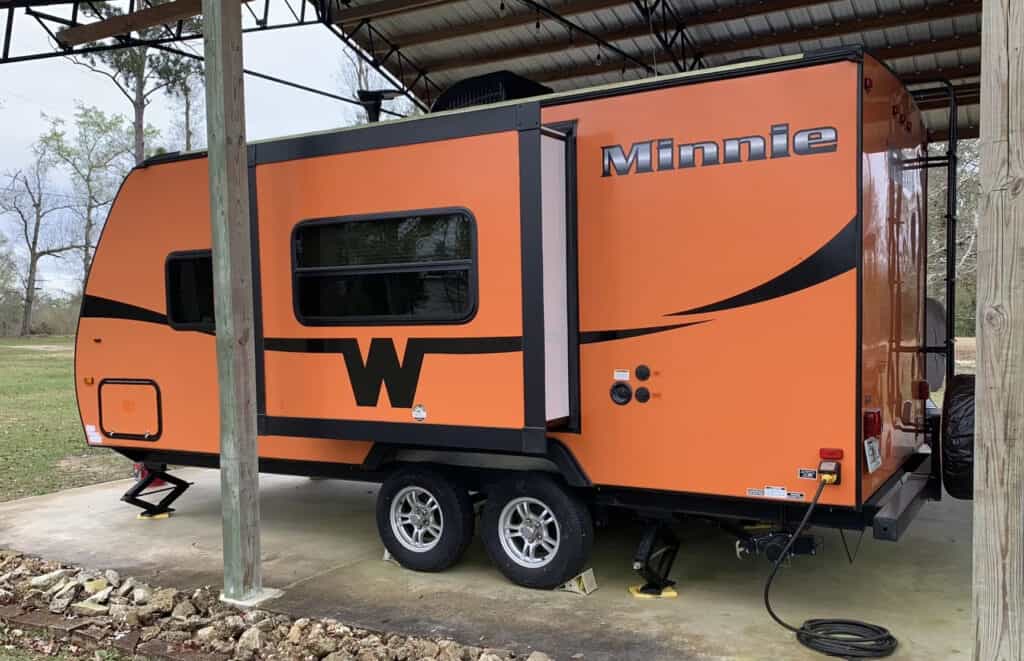 an orange Minnie Winnie travel trailer parked in a car port.