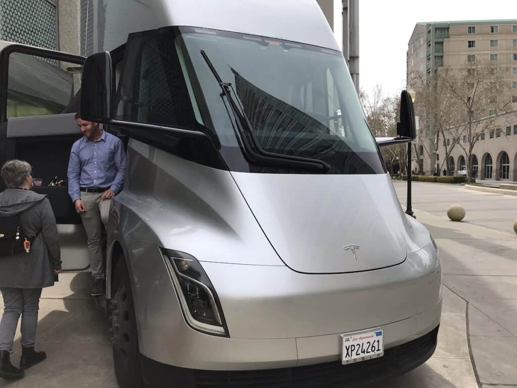 Silver Tesla Semi With a man and woman in the passenger side doorway.