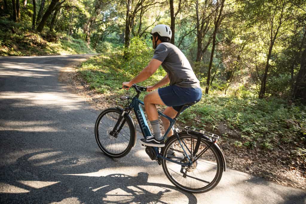 Man riding on ebikes on a cement path through the woods.