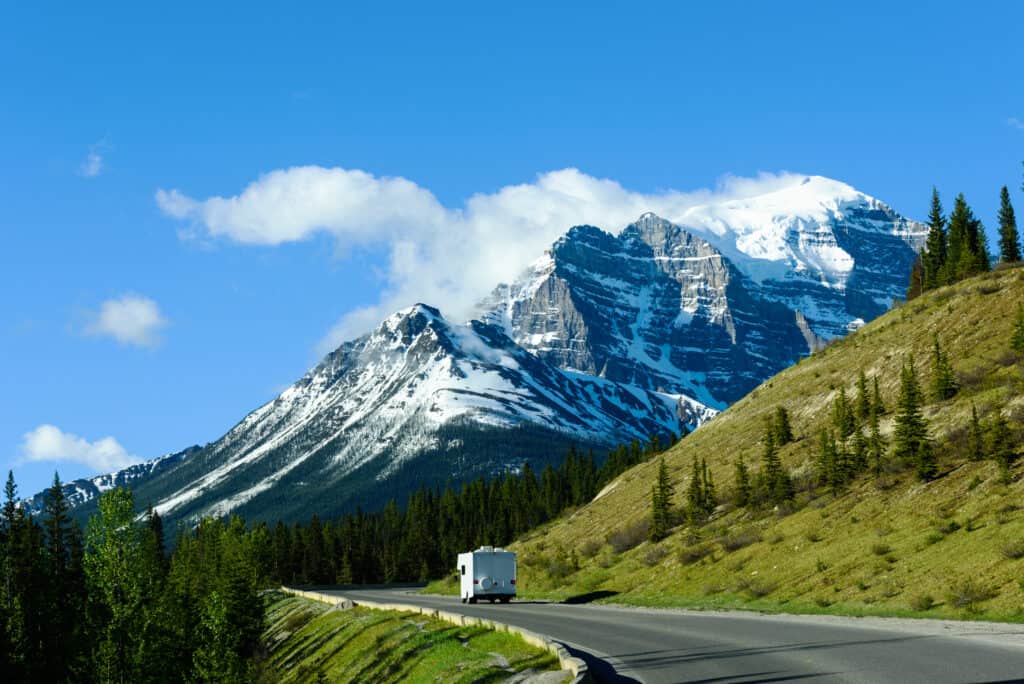 RV on highway in Canada with mountains in distance - feature image for RV Camping In Canada Tips