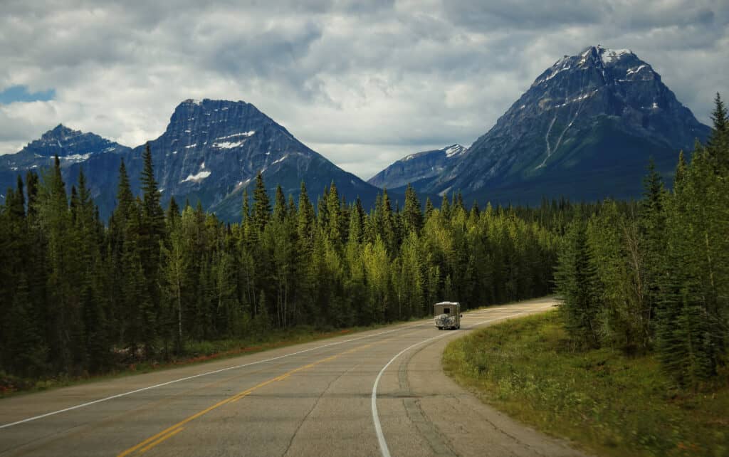 RV traveling in Canada through foreste with mountain view - feature image for Can I Travel to Canada in My RV?