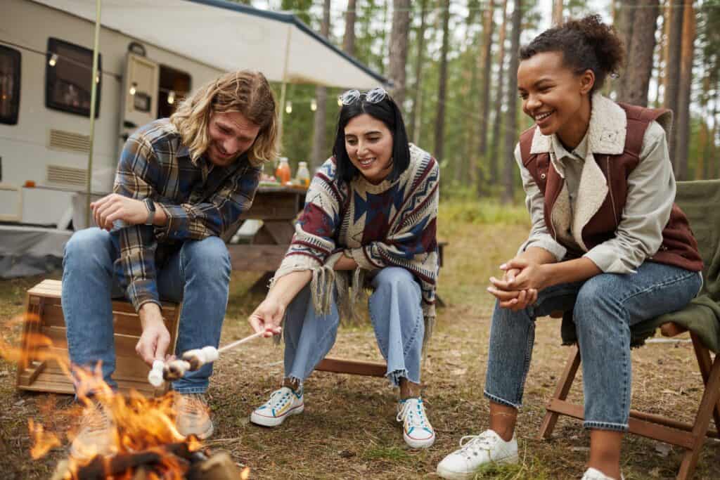 Three young adults sitting around a campfire with an RV in the background