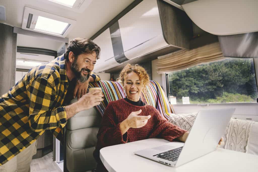 Standing bearded man and seated woman looking at laptop on table in RV