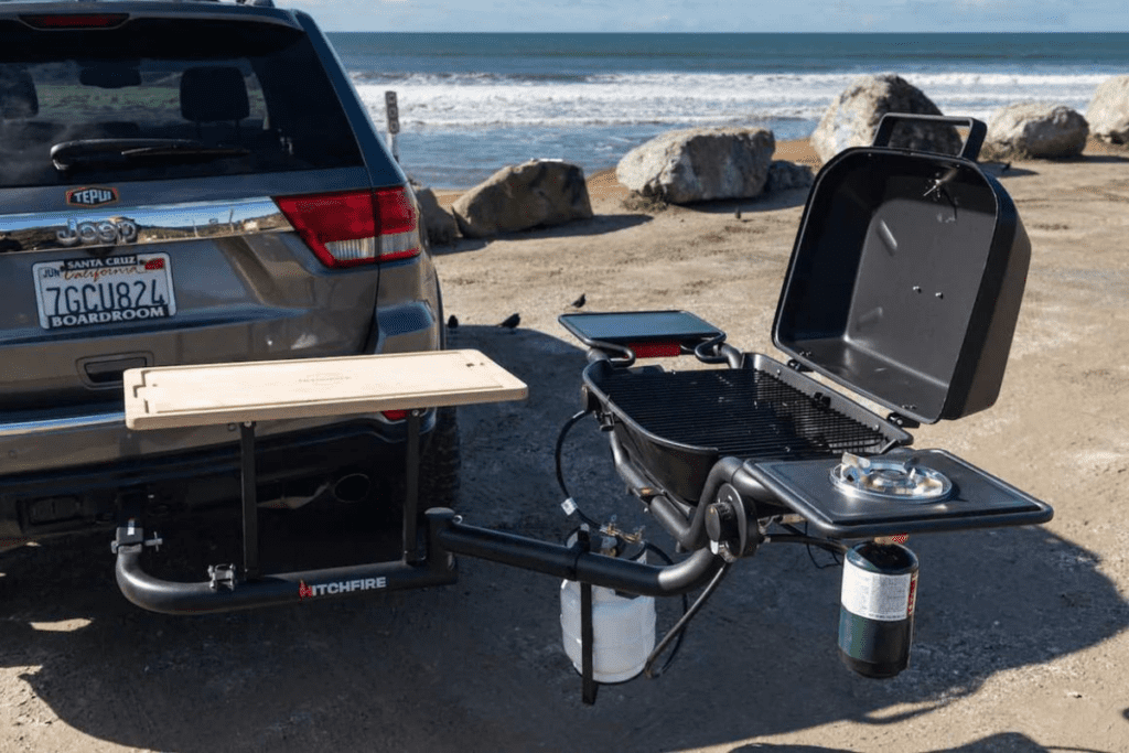SUV with hitch mounted grill and wooden cutting board parked beside the ocean - propane grill