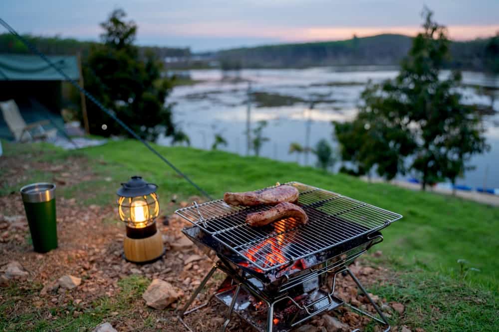 Steaks on a camp grill at a campsite near a lake.