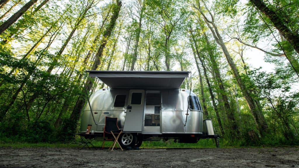 Exterior of a 2023 Airstream Bambi travel trailer in a deciduous forest  