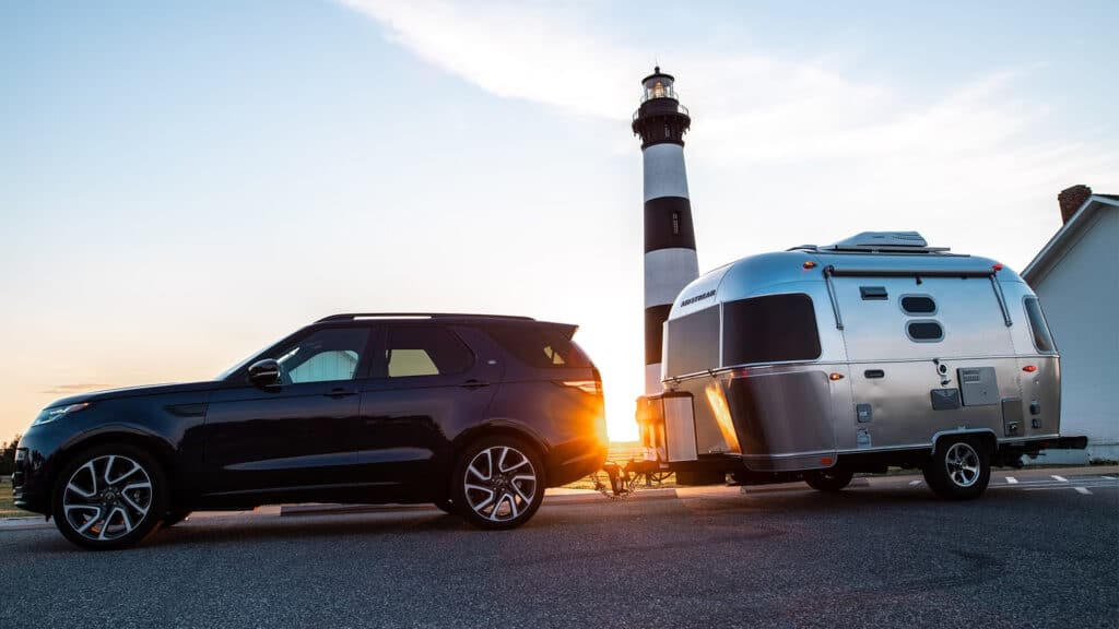 Airstream and vehicle in front of lighthouse and sunset - feature image for Airstream travel trailers 2023