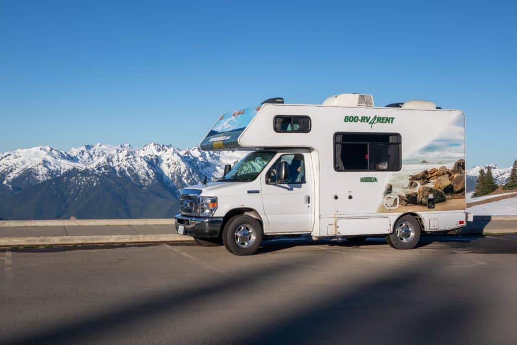 Small class B motorhome with company advertising on the side with mountains in the background - RV rental pricing