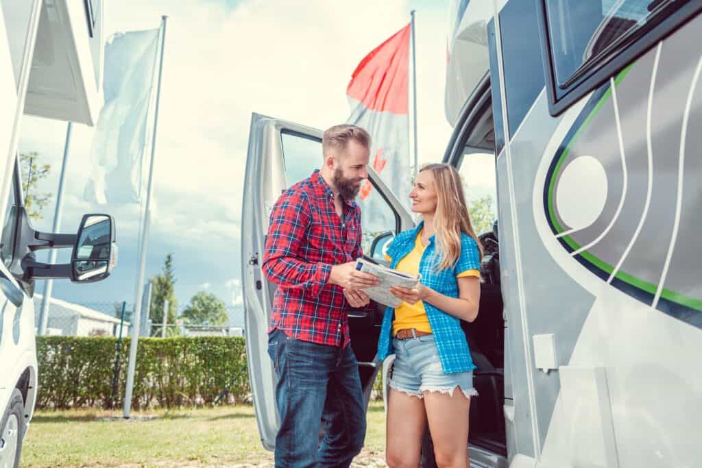 Male and female holding a road map standing outside a motorhome - RV rental pricing