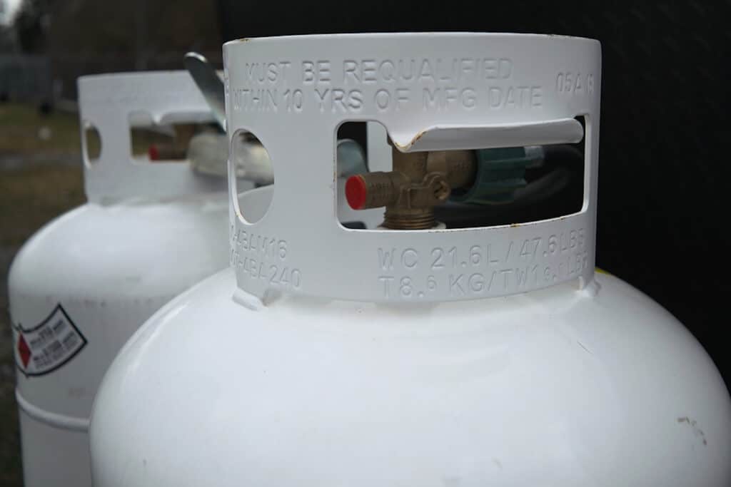 Two 20 lb RV propane tanks secured  on the front of an RV trailer
