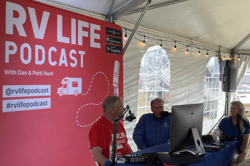 Dan Hunt, Brett Davis, and Angie Morell sit in a tented area recording the RV LIFE Podcast.