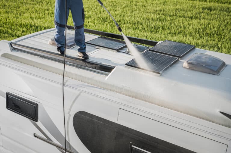 Man stands on roof of RV cleaning solar panels.