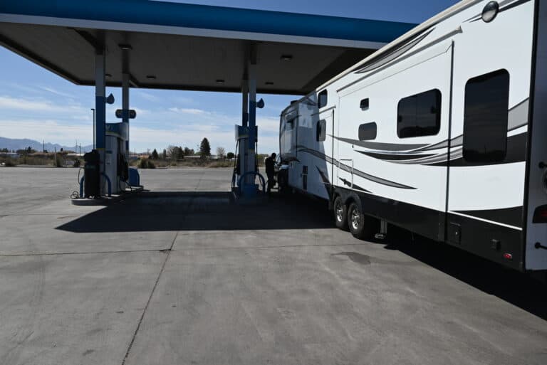 a couple of rvs parked next to each other in a parking lot with a gas station in the background, image for fuel efficiency tips