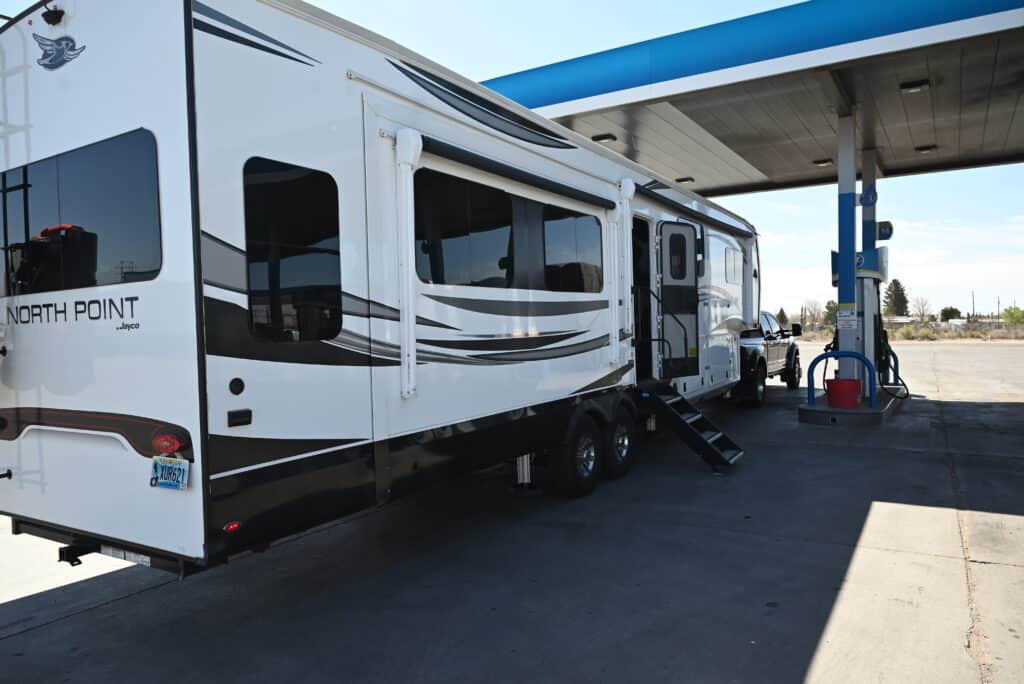 a white and black camper parked at a gas station with a blue and white gas pump in the background, image for gas efficiency 