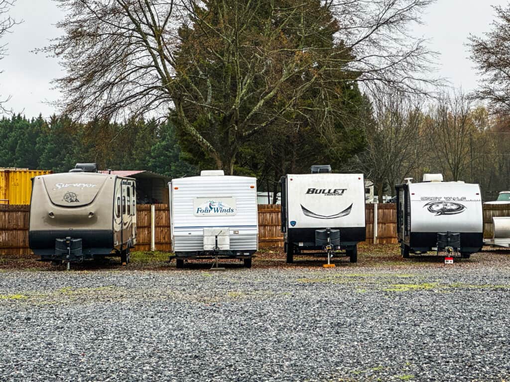 a row of travel trailers parked next to each other in front of a wooden fence with trees in the background