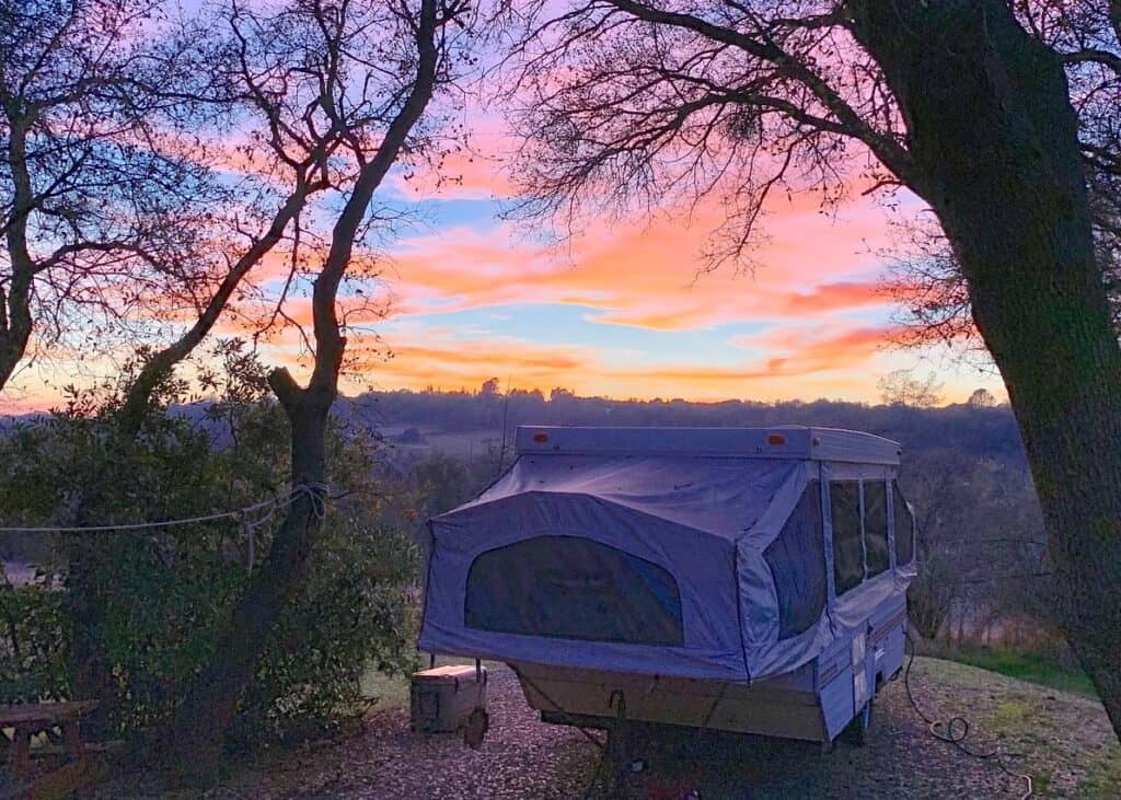 A pop-up camper at sunset overlooking a scenic valley.