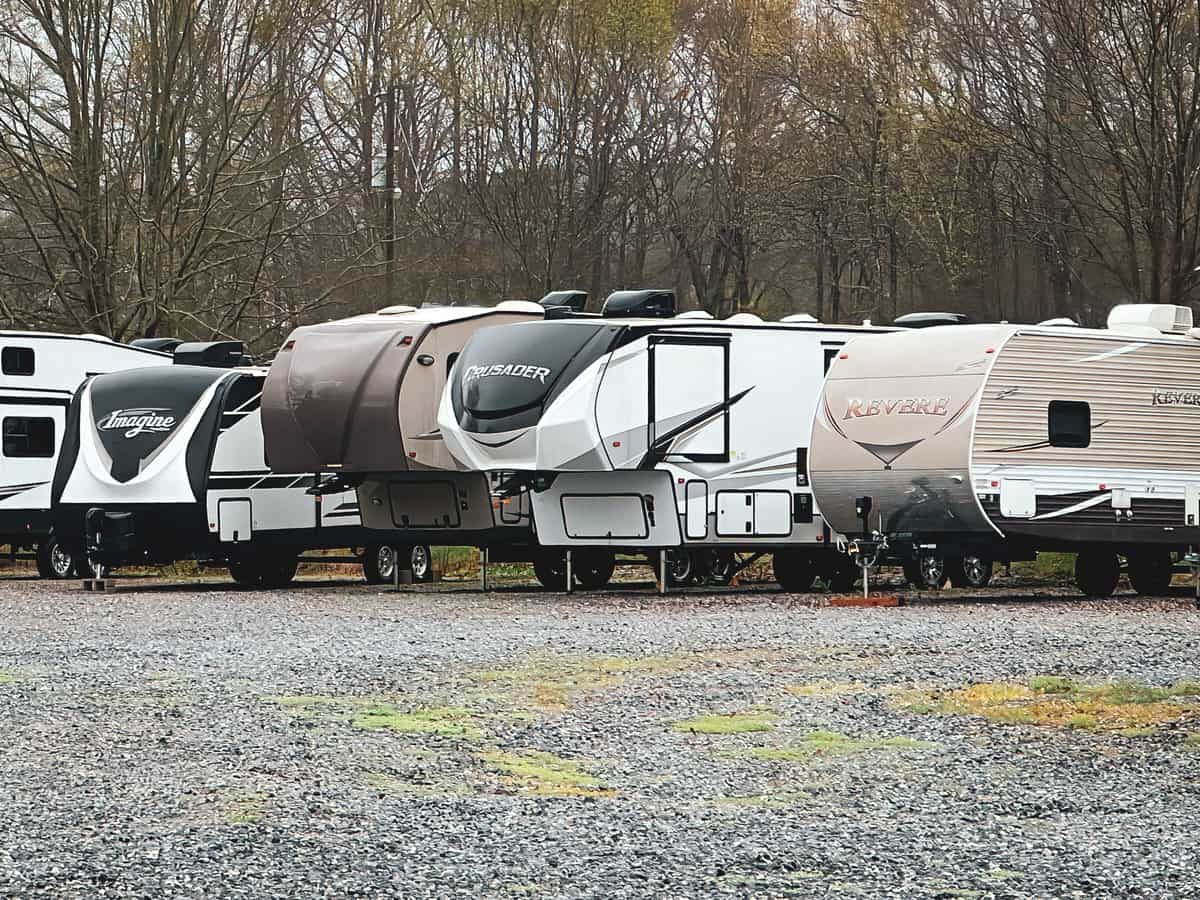 5th wheel and travel trailers sit in an rv storage lot.