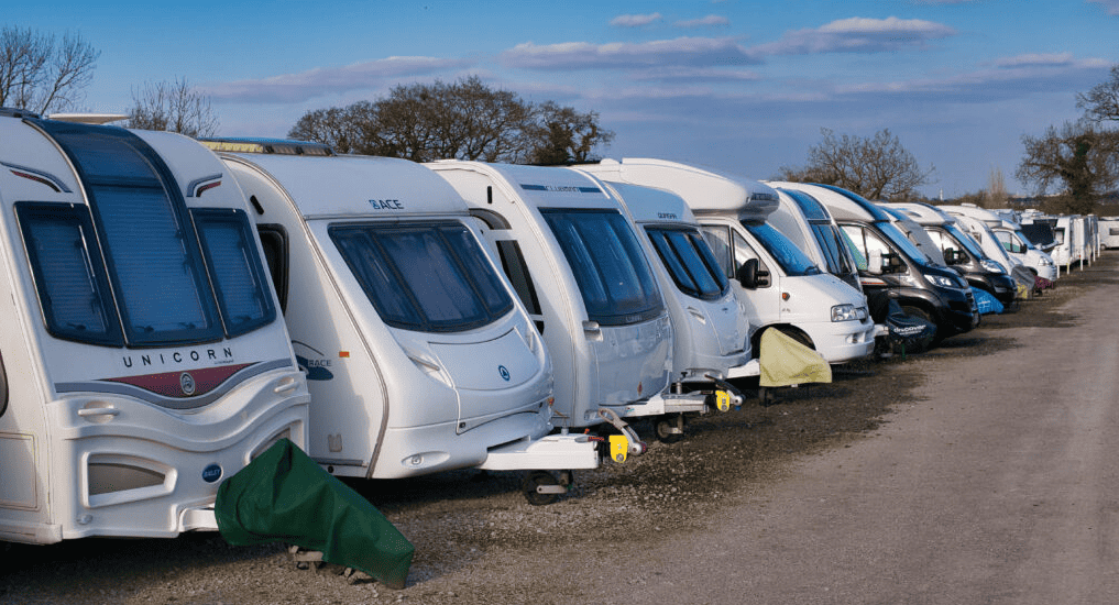 Tightly packed travel trailers and small motorhomes parked in outdoor RV storage facilities.