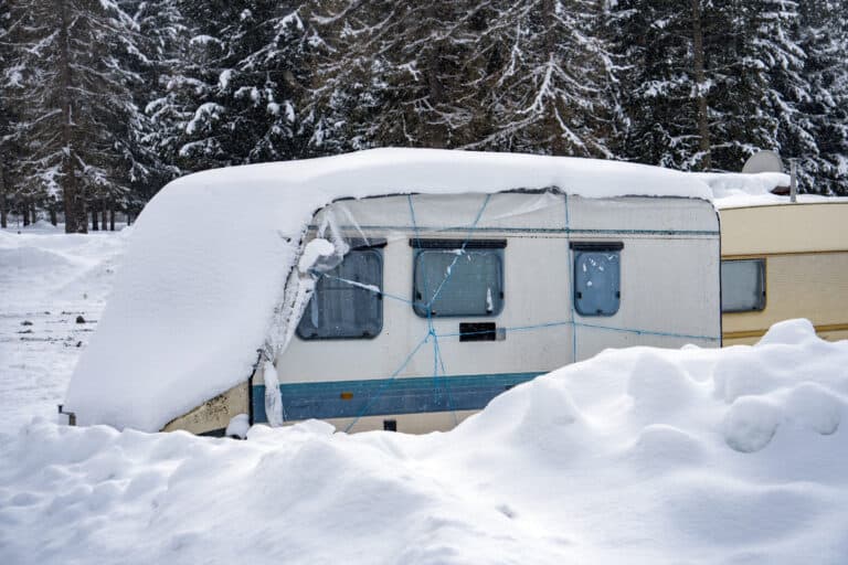 A travel trailer in winter with a partial rv cover in the snow.