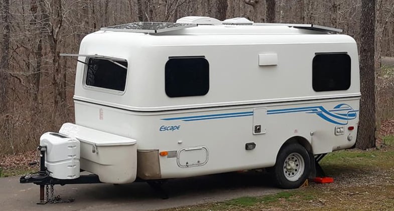 A white Escape fiberglass RV parked in a wooded area.