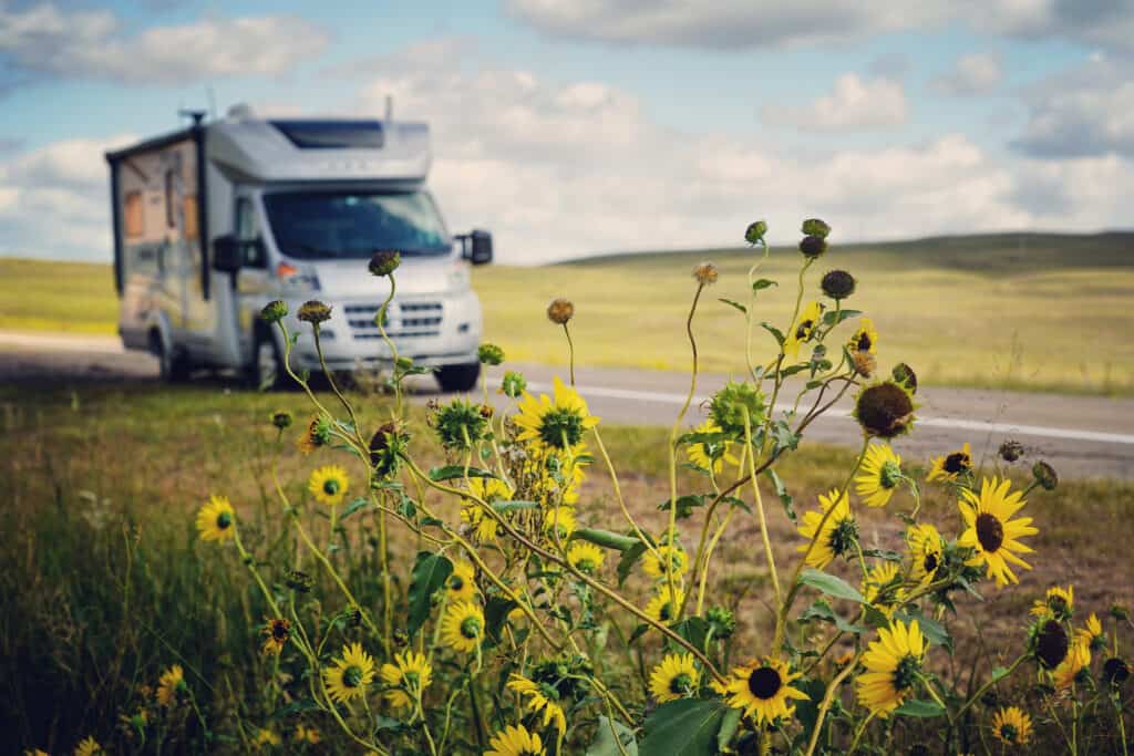 Small Class C RV on side of road looking at wild flowers in foreground.