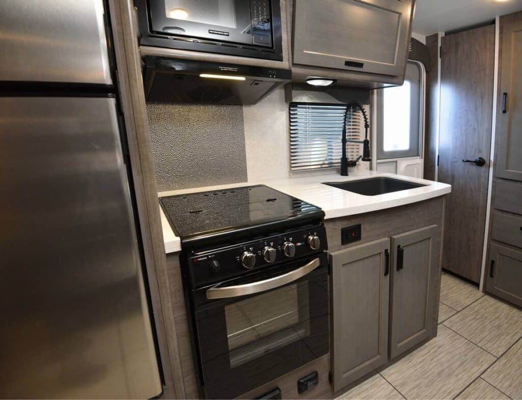 Squire travel trailer galley includes range, stovetop, microwave, and sink with high-rise faucet.